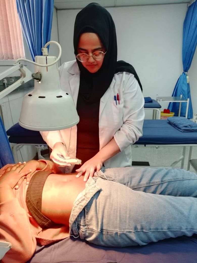 Dr Patel in a white coat giving an abdominal treatment under a heat lamp