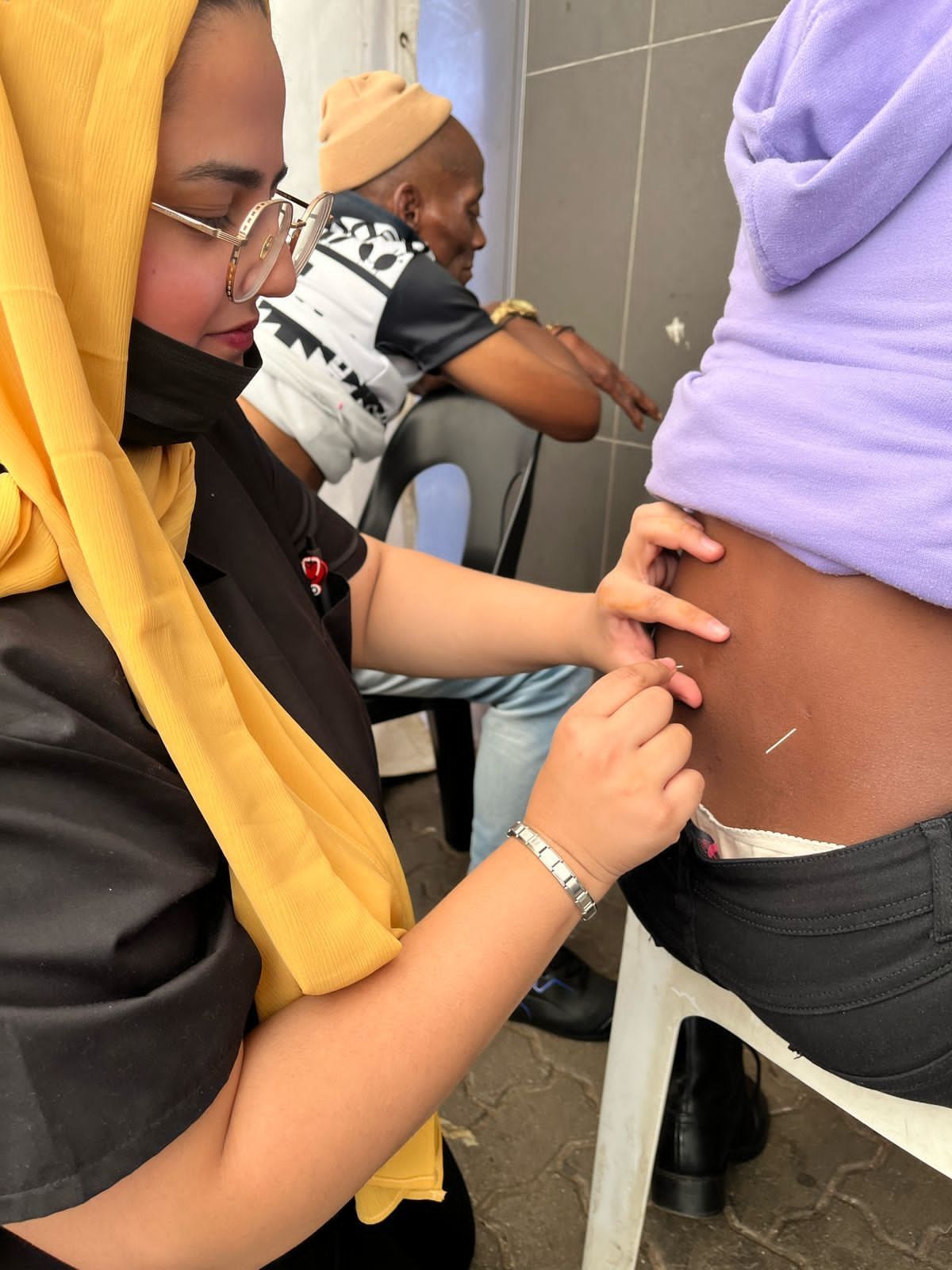 Dr Patel needling the lower back of a seated patient at a community outreach event