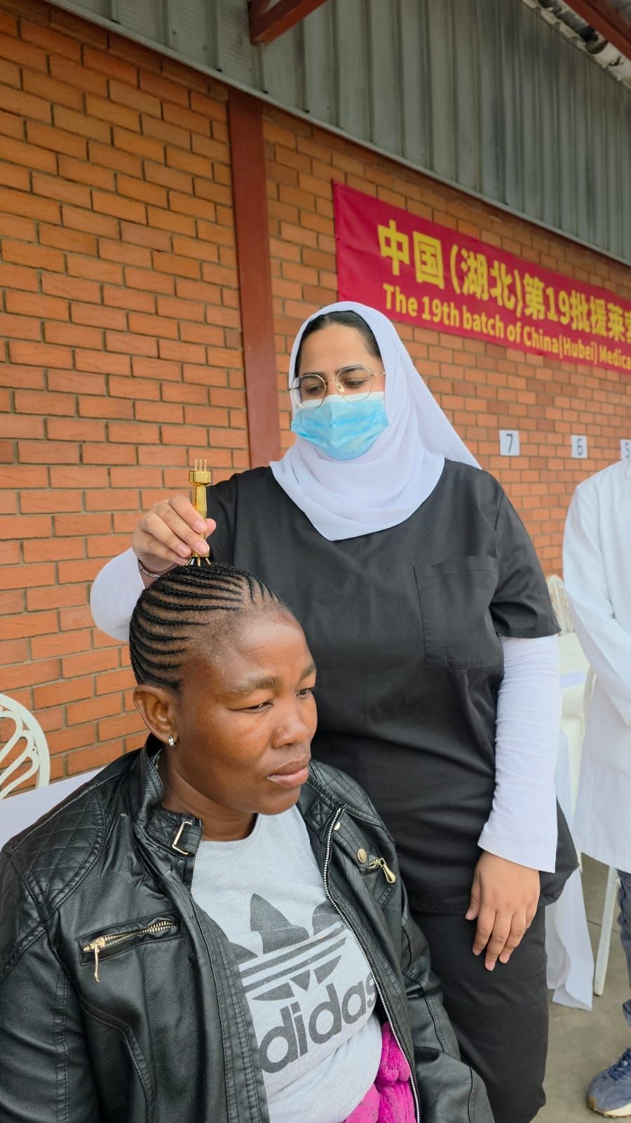 Dr Patel, wearing a mask, applying a golden pestle needle instrument to the crown of a seated patient’s head
