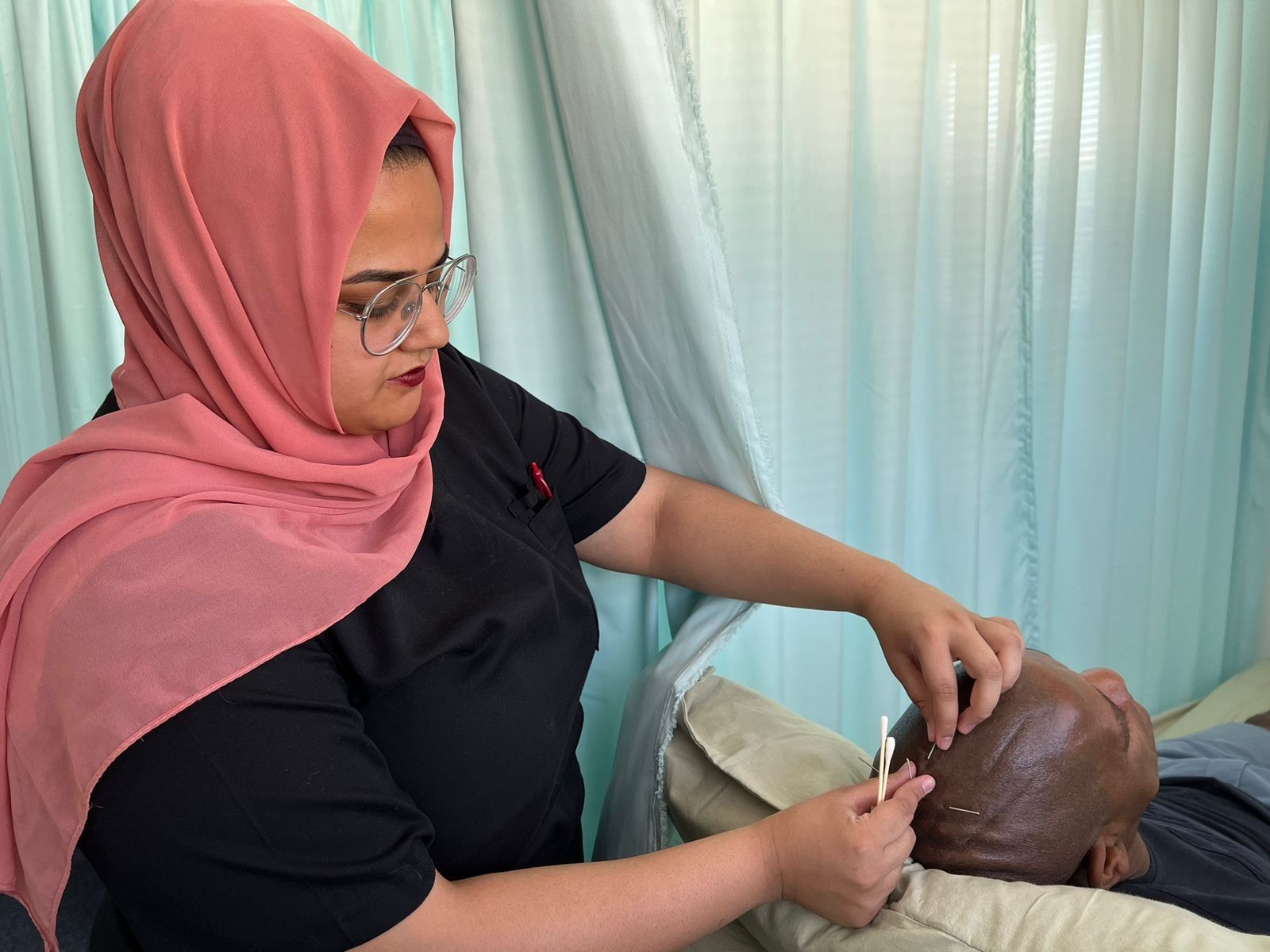 Dr Patel placing fine acupuncture needles along the scalp of a patient resting on a treatment bed